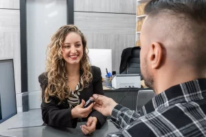 A happy woman is receiving the keys to her new car from the car dealership salesman